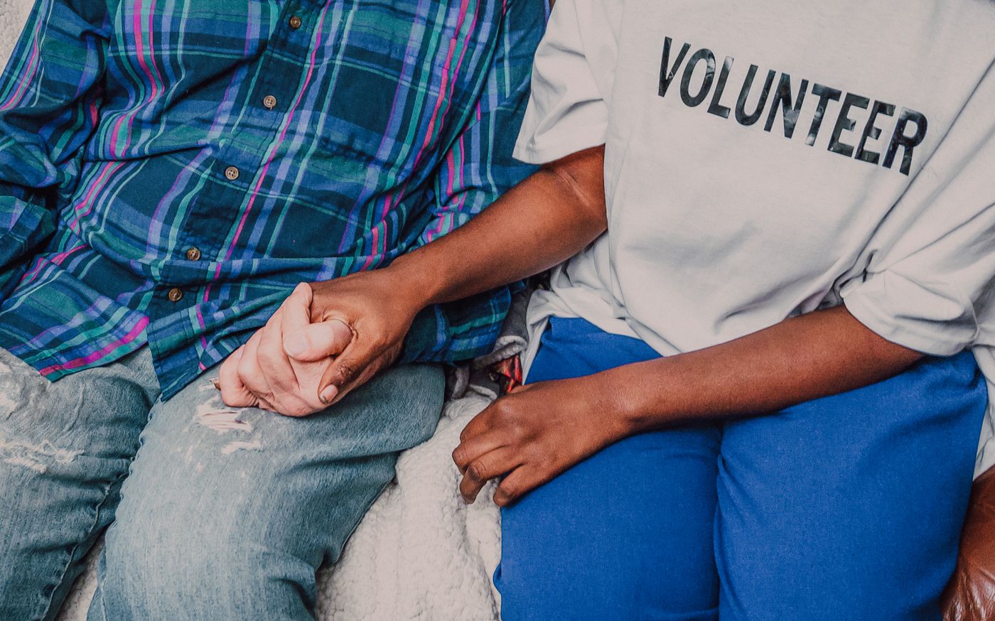 A volunteer in a Volunteer shirt holding an older person's hand